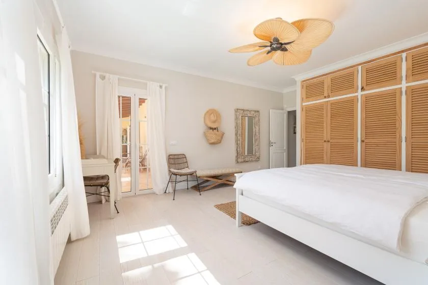 A bright bedroom with a large bed and louvered wooden cabinets.