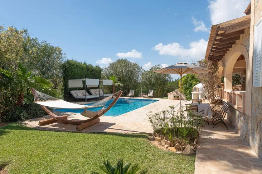 Outdoor poolside patio with lounge seating, an umbrella, and surrounding greenery.