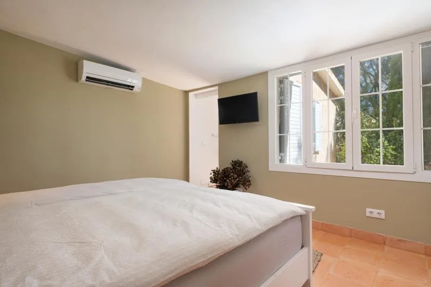 A bedroom with a bed, wall-mounted television, and large windows.