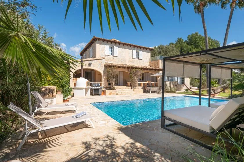 A swimming pool beside a stone house, with lounge seating and a shaded canopy.