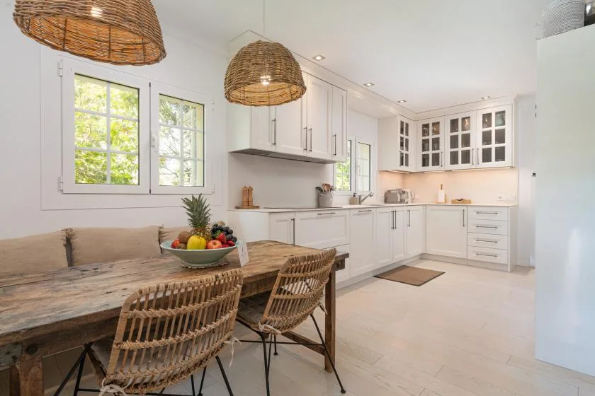 A bright kitchen and dining area with white cabinets and a wooden table.