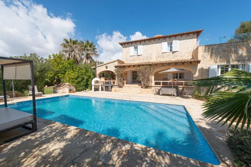 An outdoor swimming pool in front of a two-story house, with patio seating.