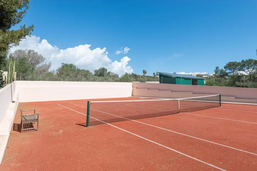 An outdoor tennis court with a net and red playing surface.