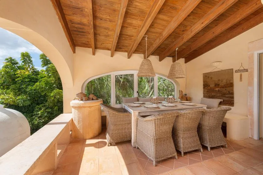 A covered outdoor dining area with a table and wicker seating.