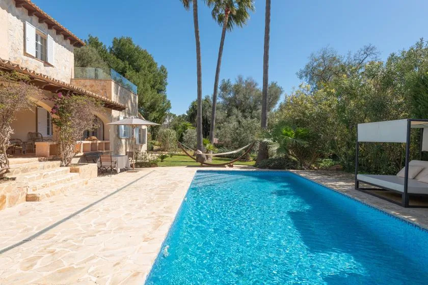 An outdoor swimming pool beside a stone patio, with trees and a hammock nearby.