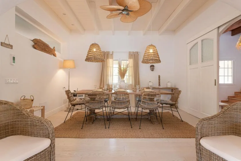 A bright dining area with a long table, woven seating, and pendant lights.