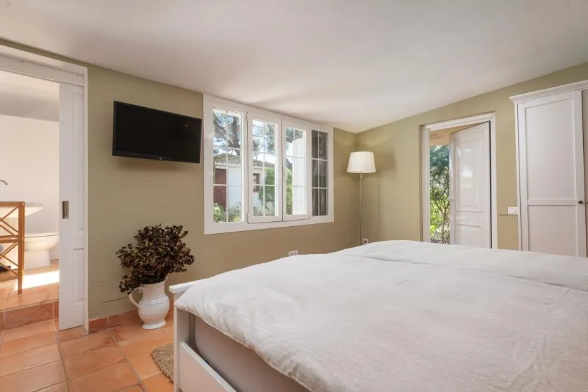 A bedroom with a large bed, windows, and a television on the wall.
