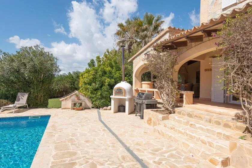 Un patio soleado junto a una piscina cuenta con una zona de comedor al aire libre a la sombra.