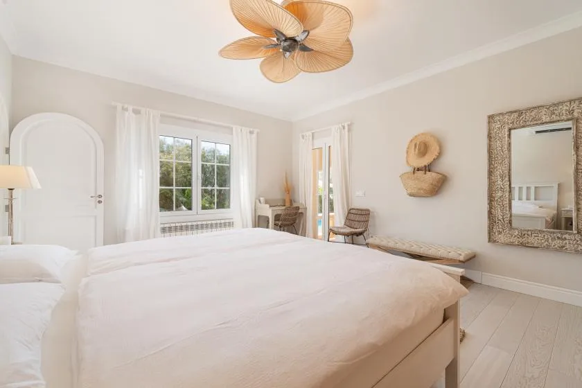 A bright bedroom with a large bed, white curtains, and a ceiling fan.