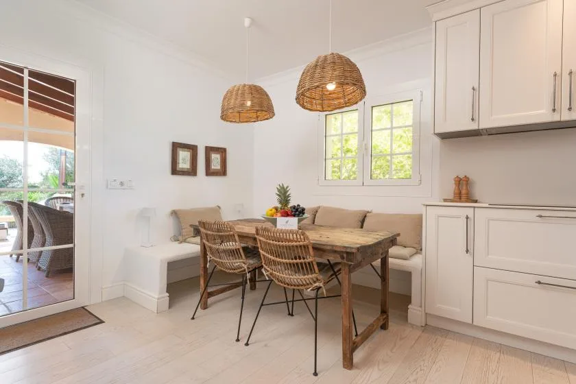 A bright dining area with a wooden table, woven seating, and windows.