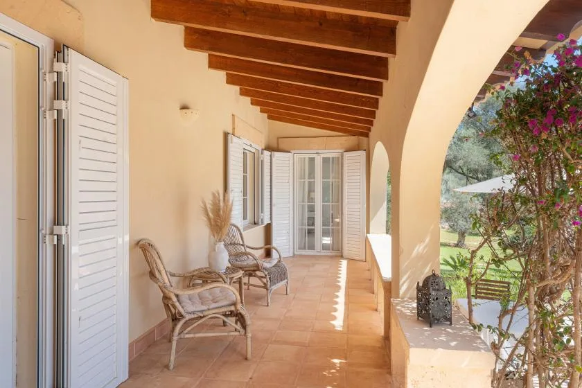 A covered terrace with seating and open white shutters along the wall.
