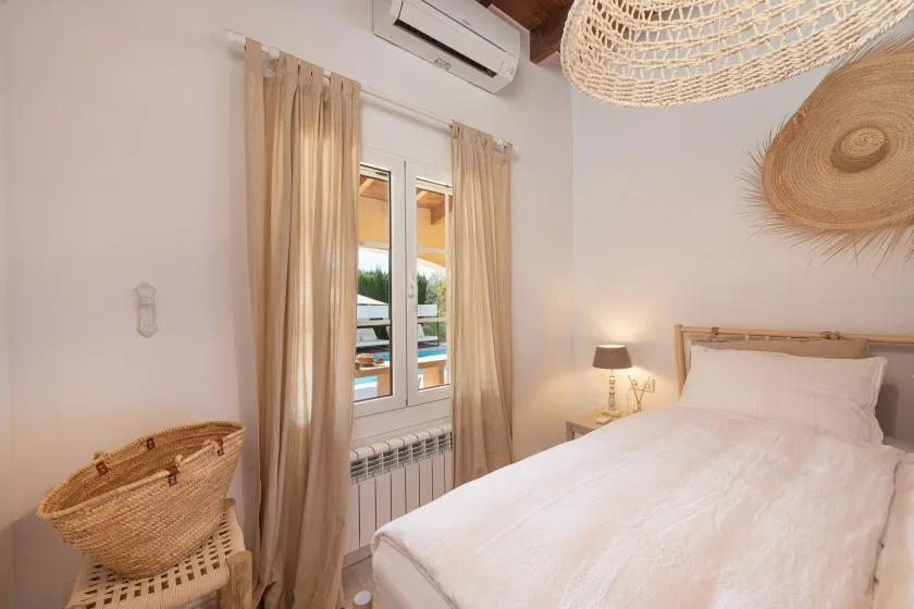 A bright bedroom with a white bed, curtained window, and woven wall decor.