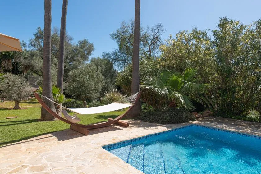 Una piscina al aire libre junto a una hamaca y un jardín cuidado.