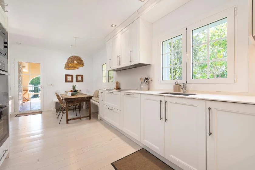 A bright kitchen with white cabinets, a sink, and a dining table.
