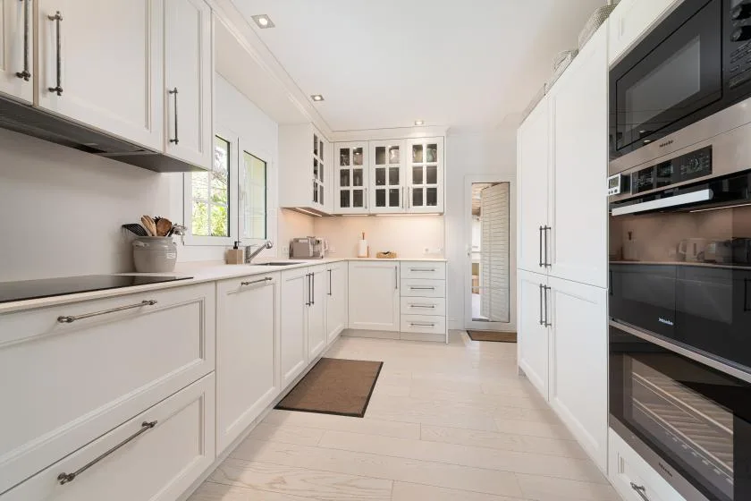 A bright white kitchen with cabinets, countertops, and built-in appliances.