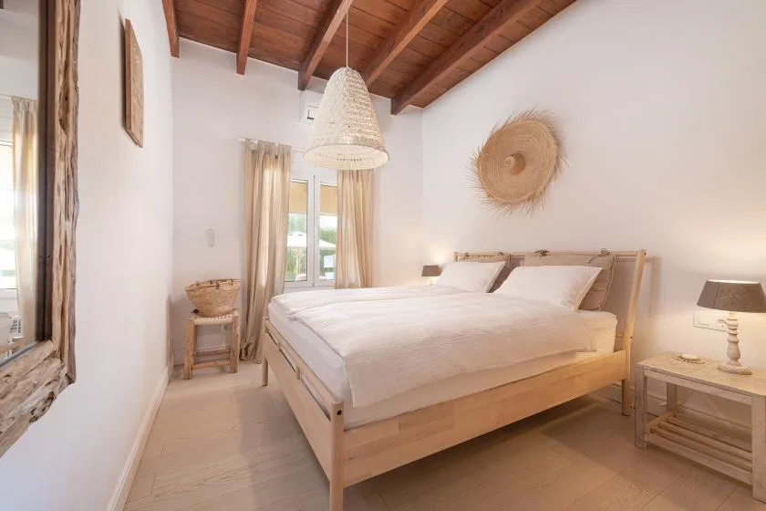 A bright bedroom with a wooden bed, white bedding, and exposed ceiling beams.