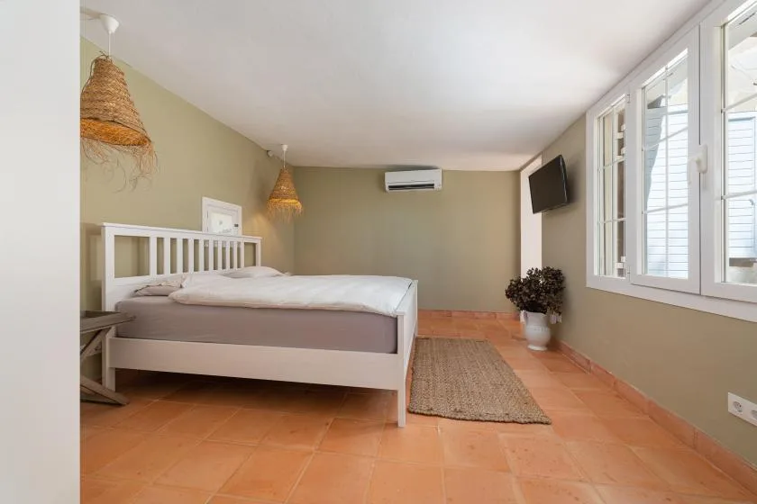 A bedroom with a bed, a woven rug, and large windows.
