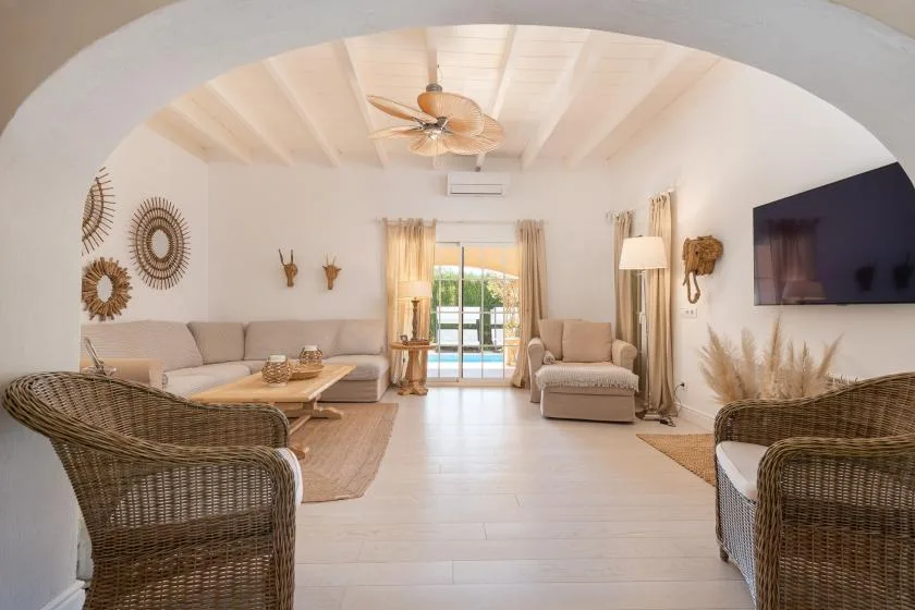 A bright living room with seating, woven armchairs, and glass doors opening to a patio.