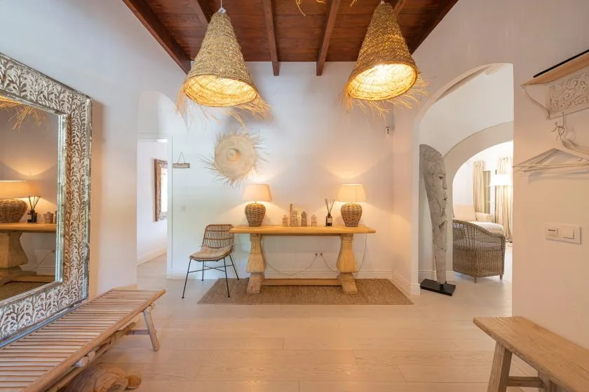 A bright dining area has a long wooden table beneath woven pendant lights.