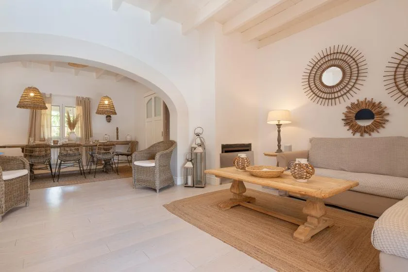 A bright living room with a wooden coffee table and seating beside an arched dining area.