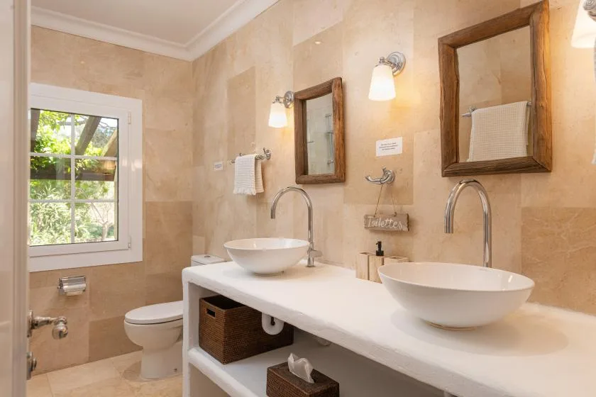 A tiled bathroom with a long vanity, two vessel sinks, and a window.
