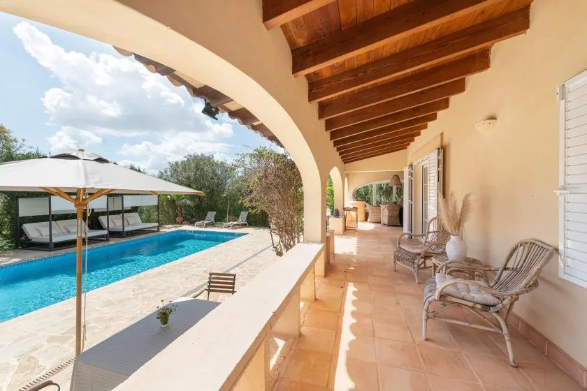 A covered outdoor terrace overlooks a swimming pool, with seating along the wall.