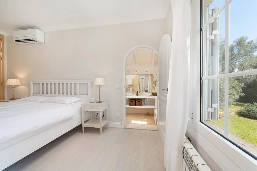 A bright bedroom with a bed, bedside tables, and a large window.