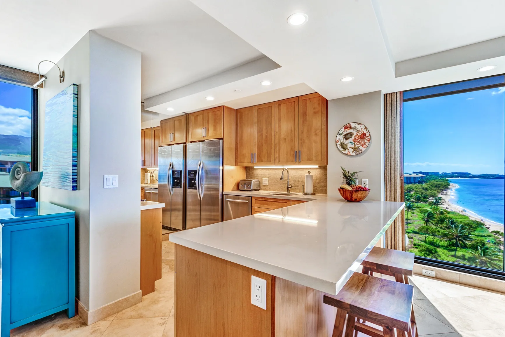 A bright kitchen with a large island, wooden cabinets, and ocean views through the windows.