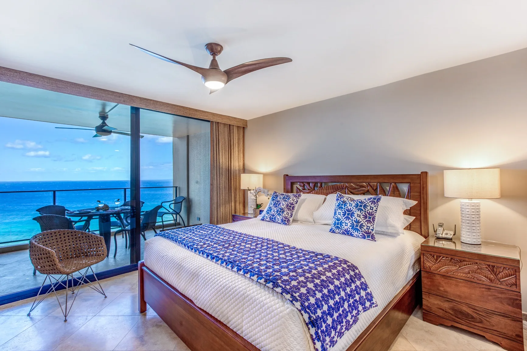 A bedroom with a large bed beside glass doors overlooking the ocean.