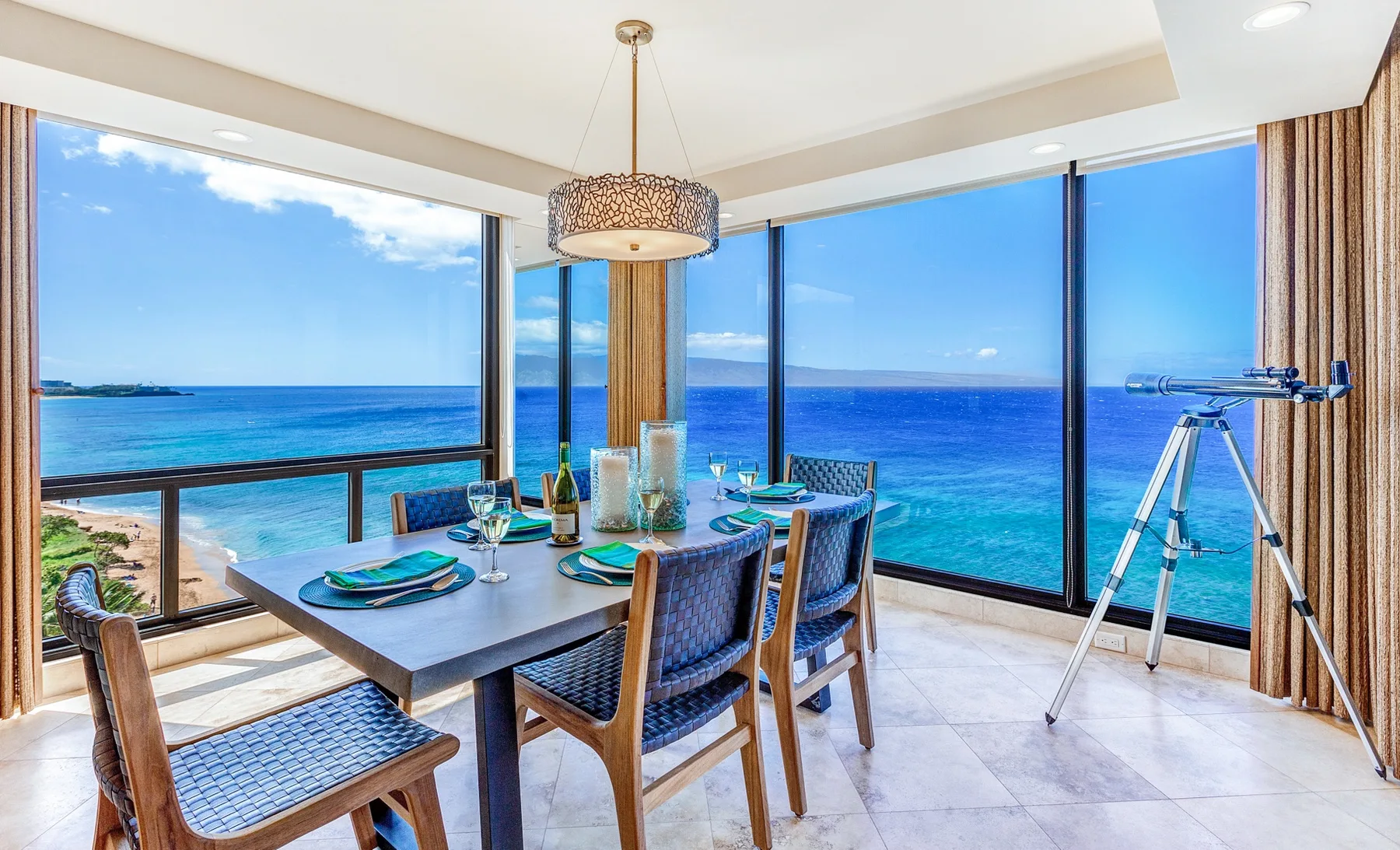 A dining area with a set table beside large windows overlooking the ocean.