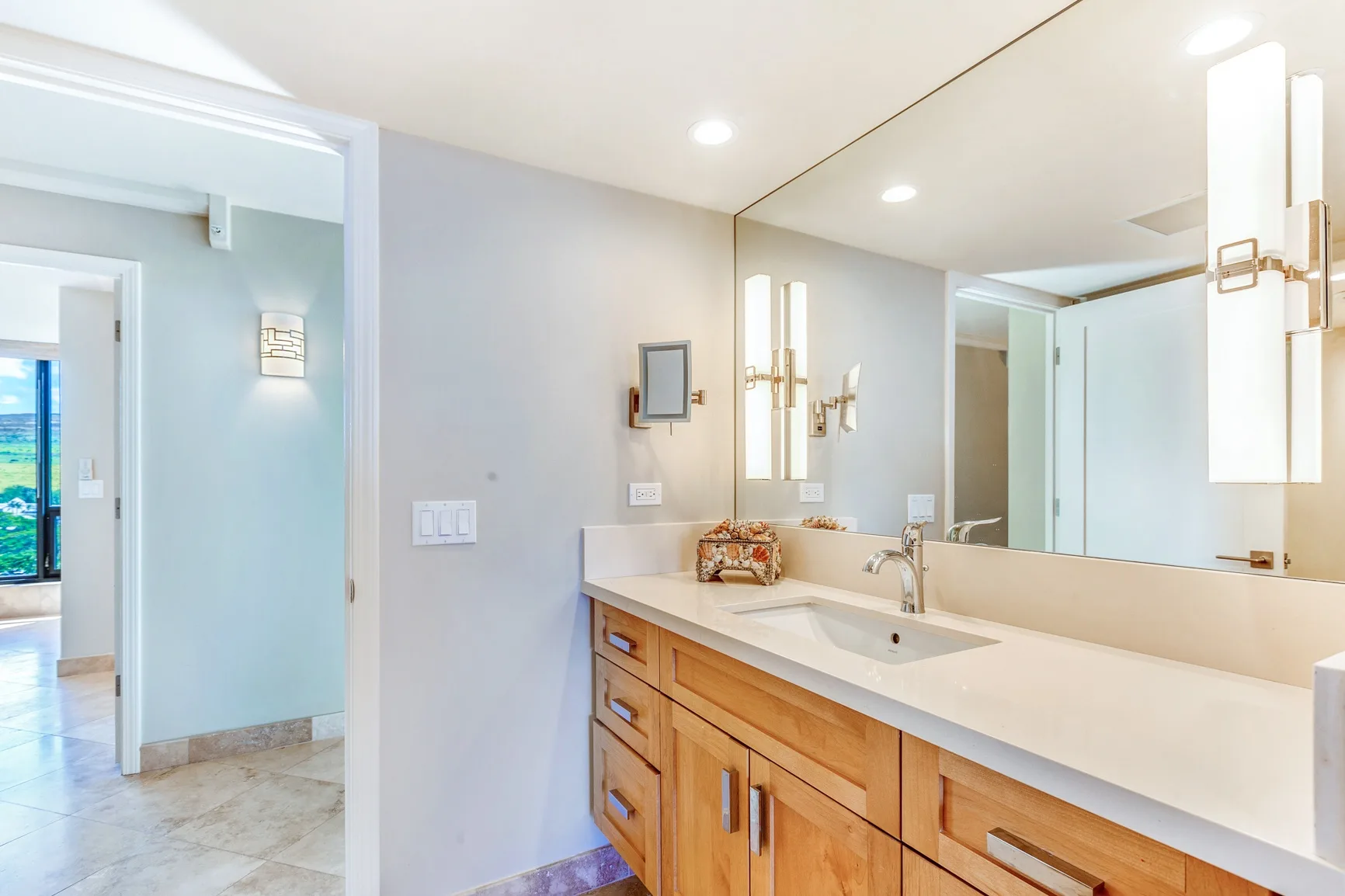 A bright bathroom with a long vanity, sink, and large wall mirror.