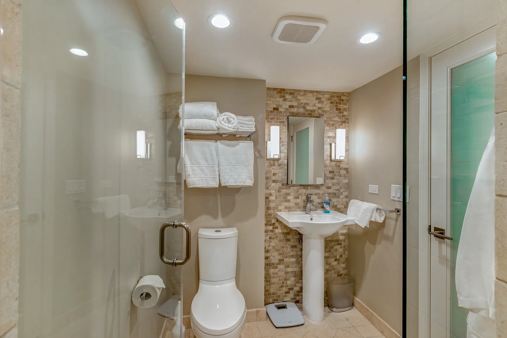 A bathroom with a shower, toilet, and pedestal sink.