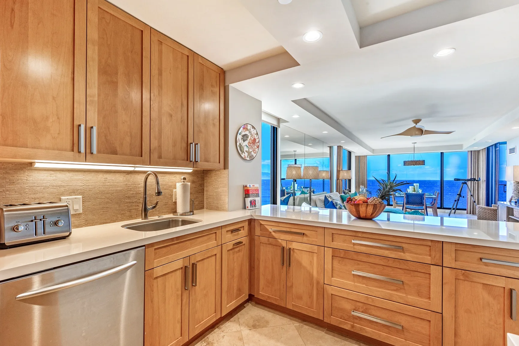 A wood-cabinet kitchen opens onto a dining and living area with large windows.