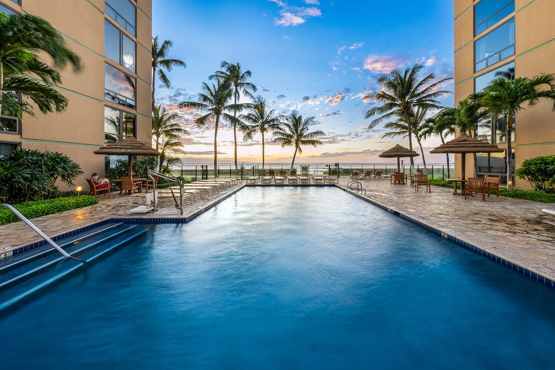 Una piscina al aire libre está entre dos edificios, con palmeras junto a la terraza.