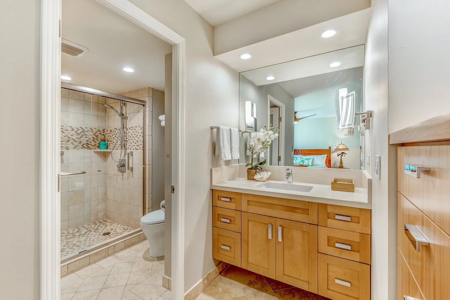A bathroom vanity with a large mirror beside a tiled shower.