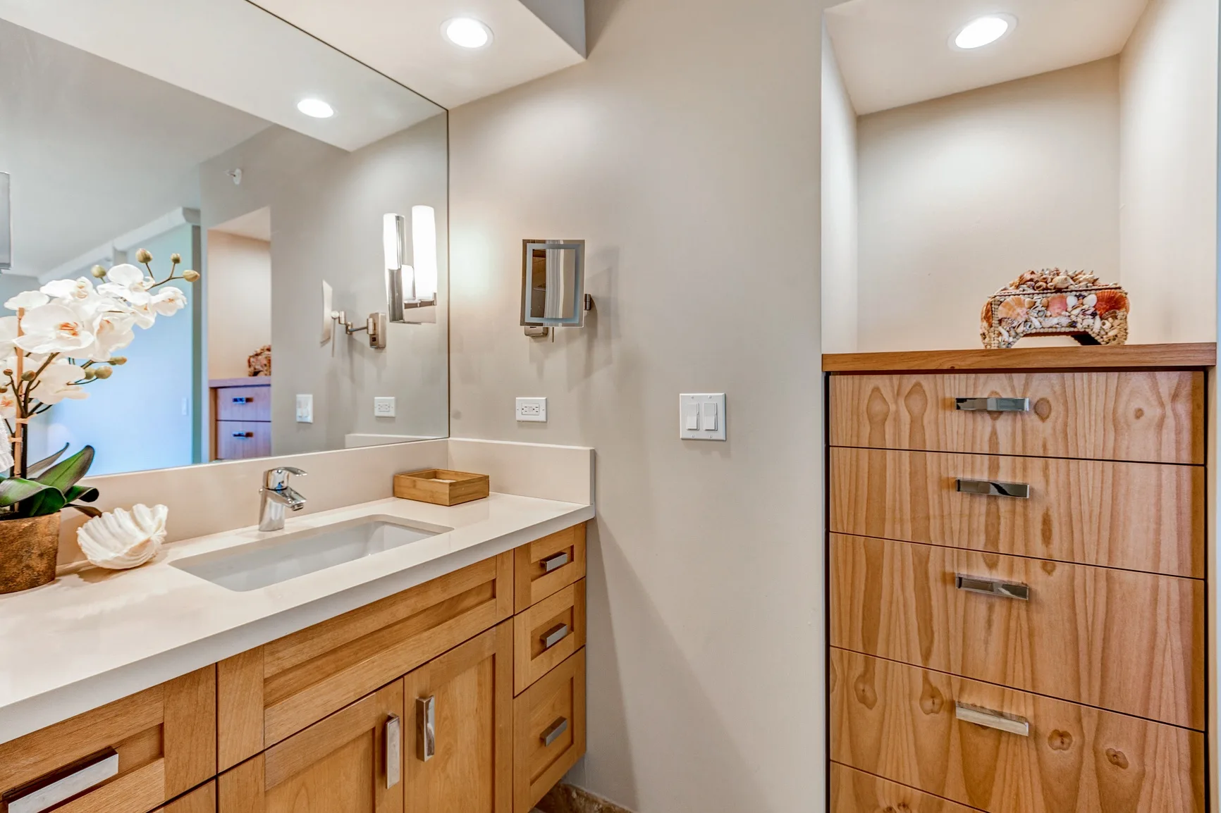 A bathroom vanity with a wide mirror and wooden cabinetry.