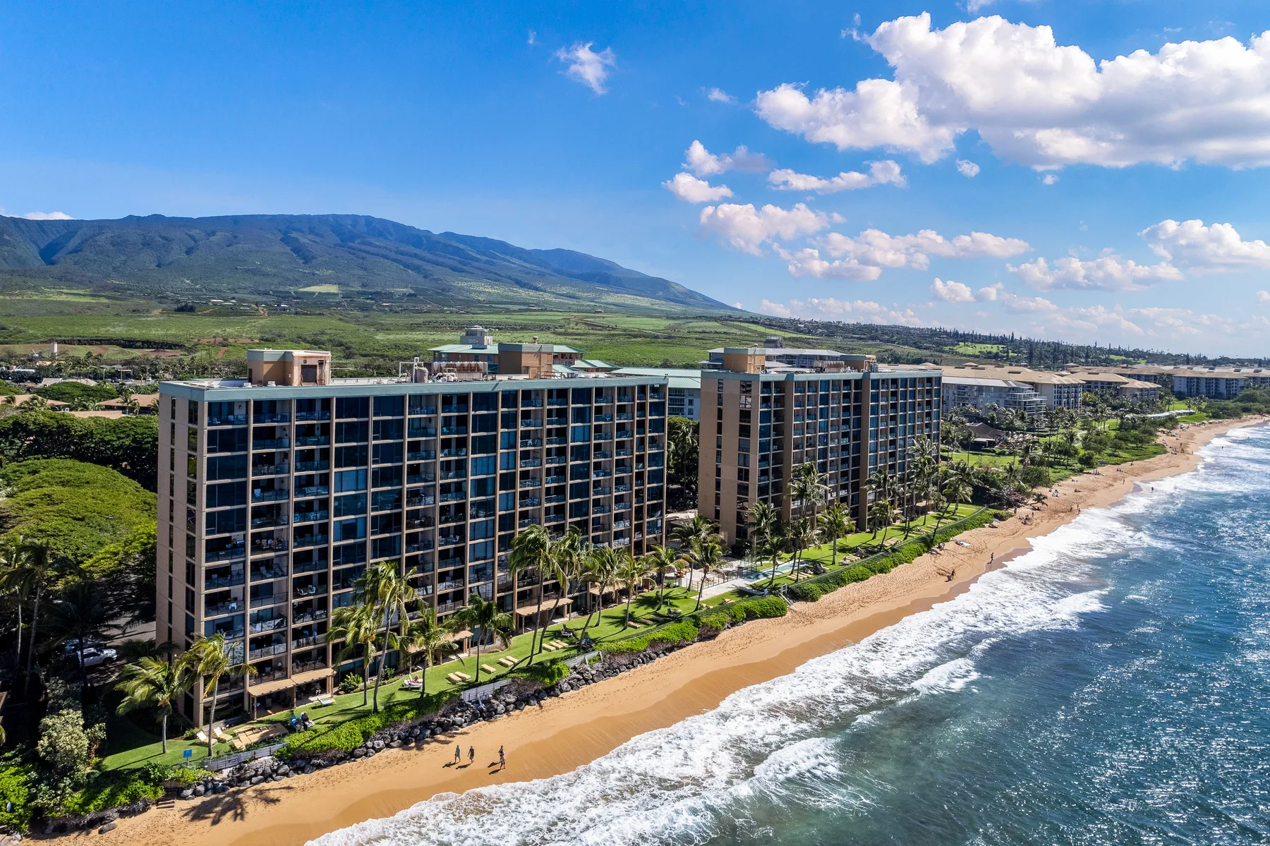 A beachfront resort building sits beside a sandy beach and ocean.
