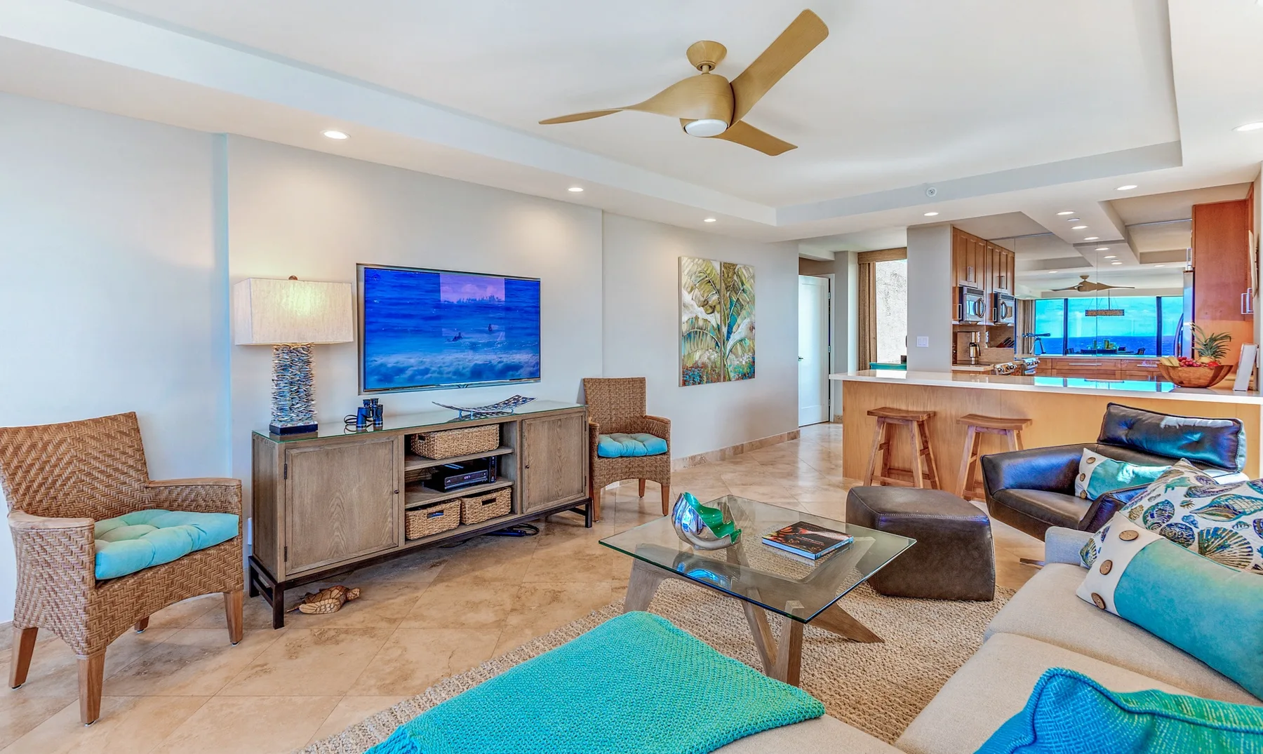 A bright living room with seating, a television, and an open kitchen.