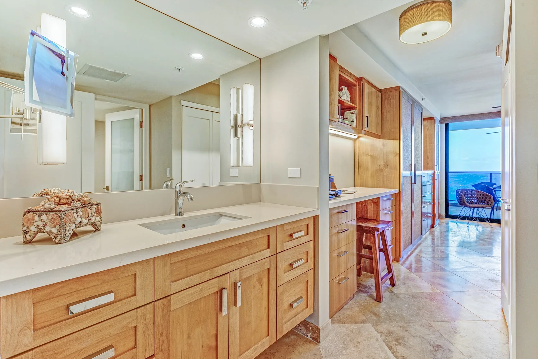 A long bathroom vanity with a sink and mirror opens onto a bright hallway.
