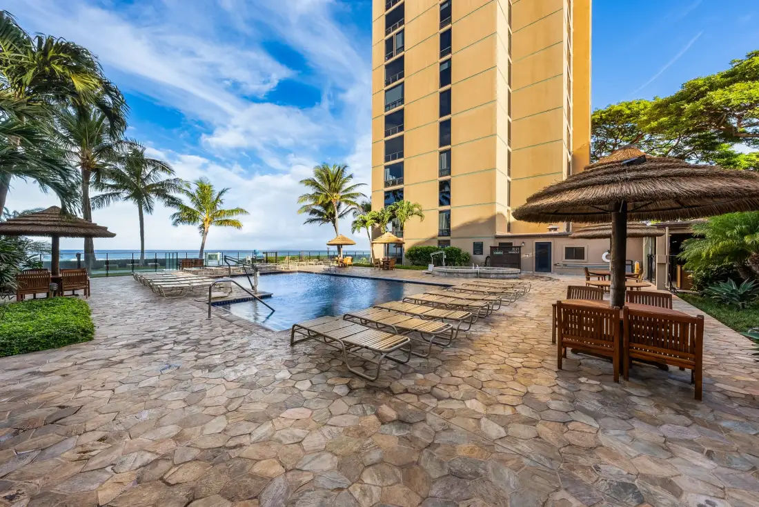 An outdoor pool deck with lounge seating, palm trees, and a tall building.