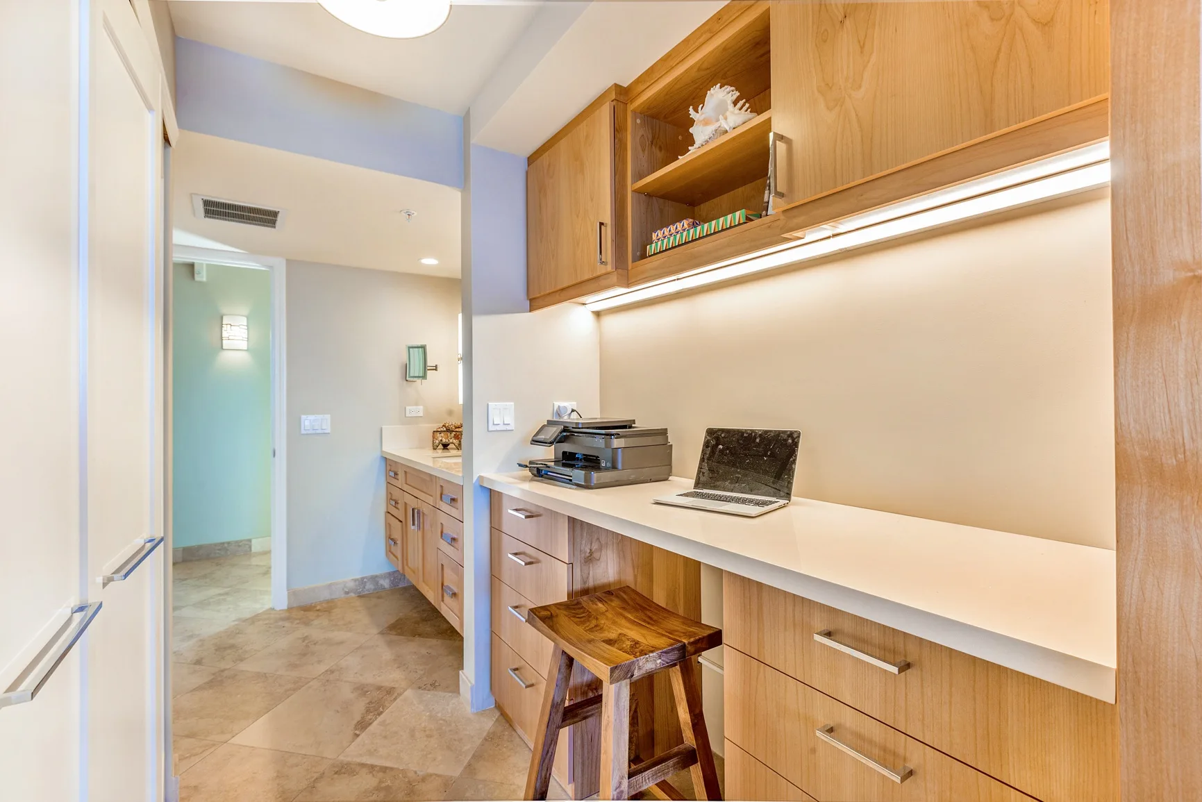 A bright office workspace with a long desk, shelving, and a wooden stool.