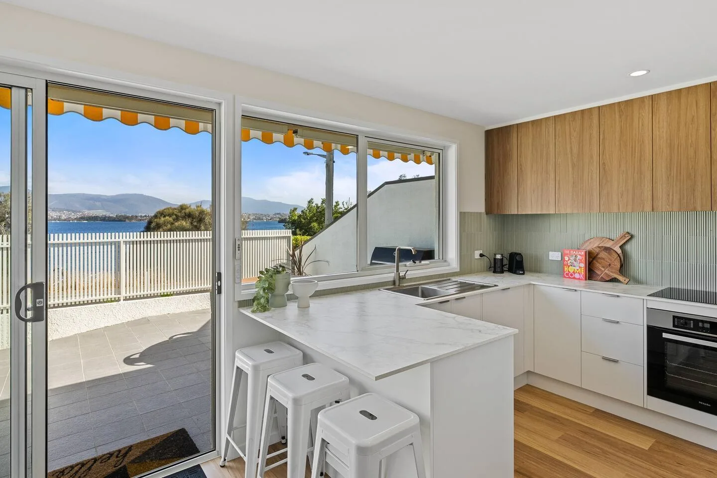 A bright kitchen has a white island with stools beside sliding glass doors.