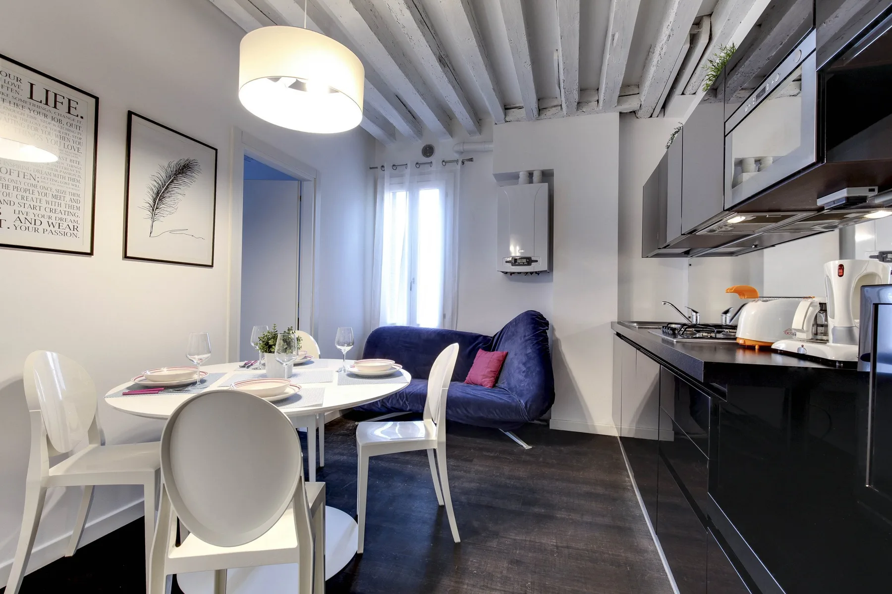 Un comedor junto a una cocina compacta, con una mesa puesta cerca de la ventana.