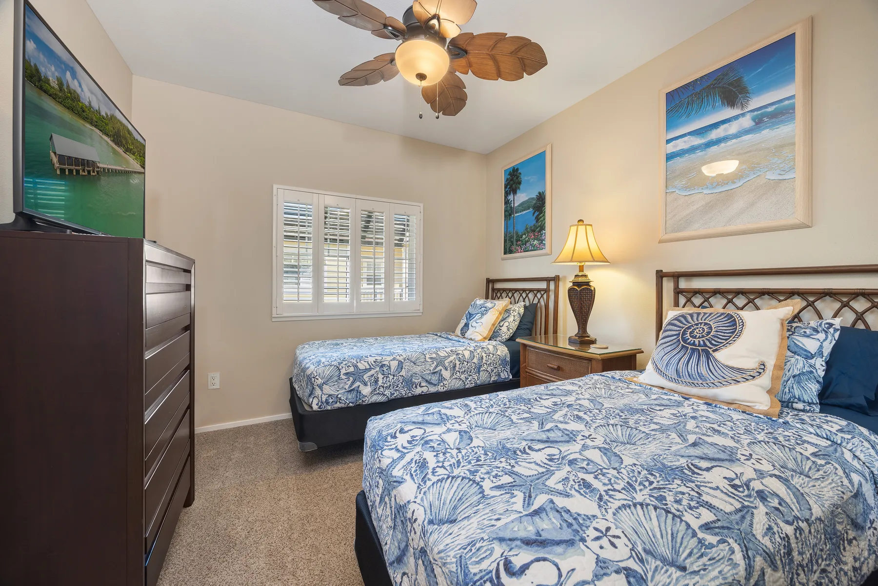 Un dormitorio con dos camas, ropa de cama estampada azul y cuadros de playa.