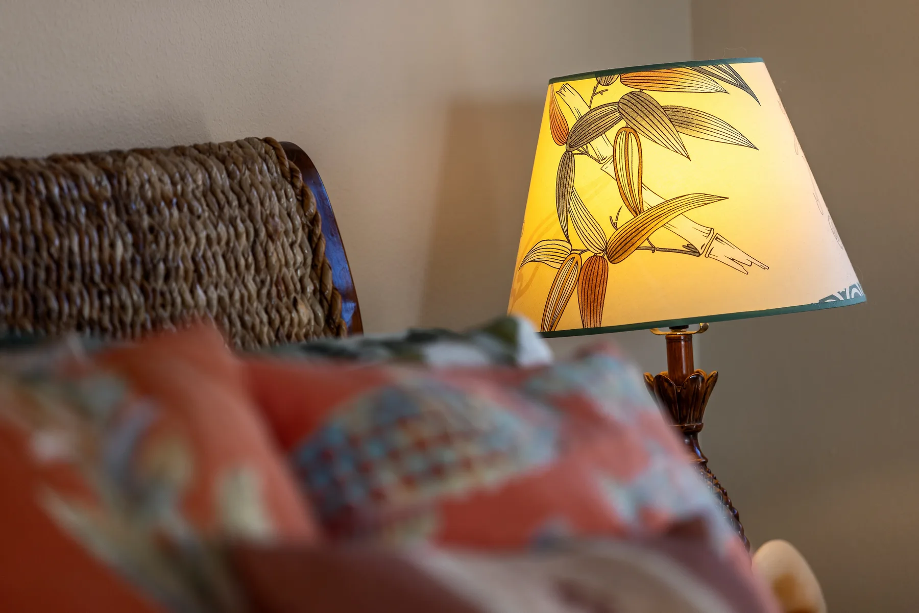Una lámpara de mesa con pantalla botánica está junto a una cama con almohadas estampadas.