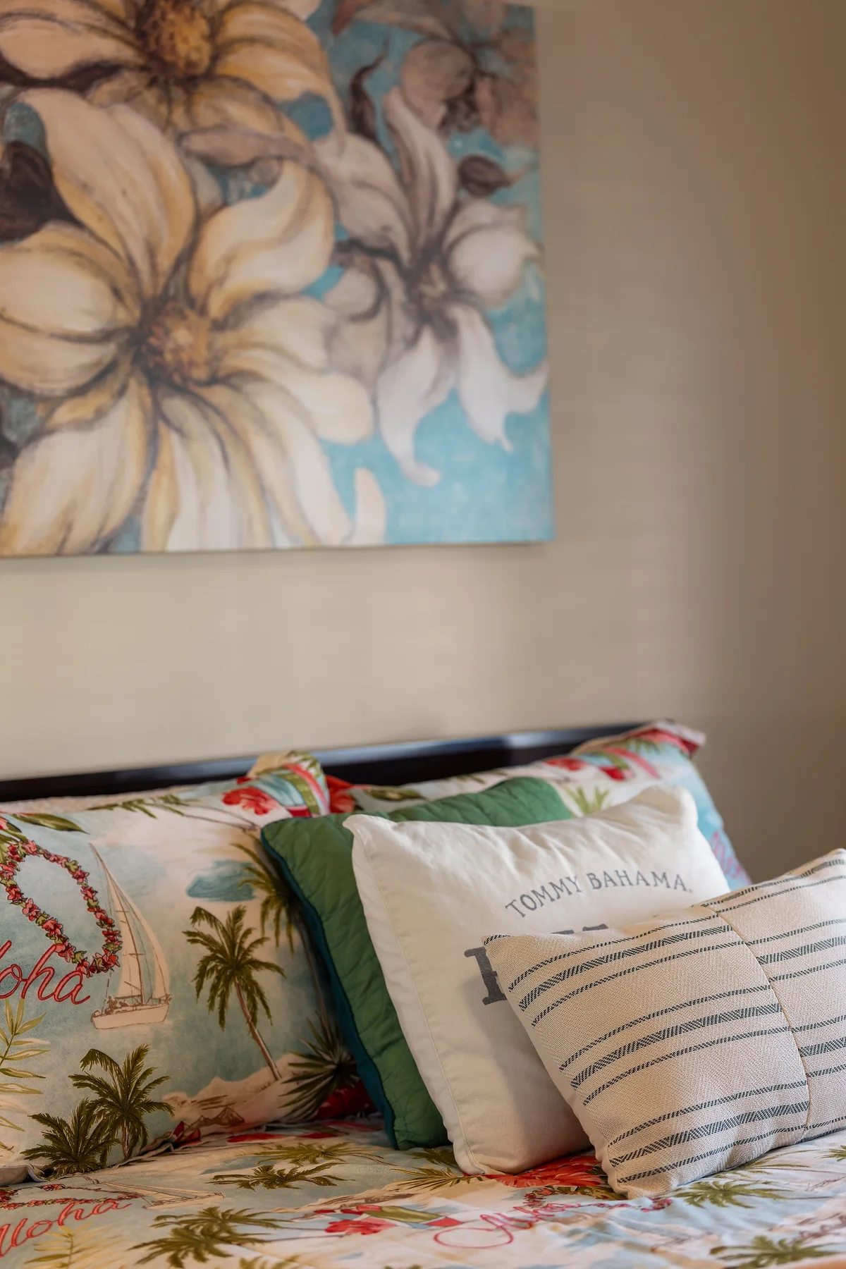 Una cama está decorada con almohadas coloridas bajo una pintura floral.
