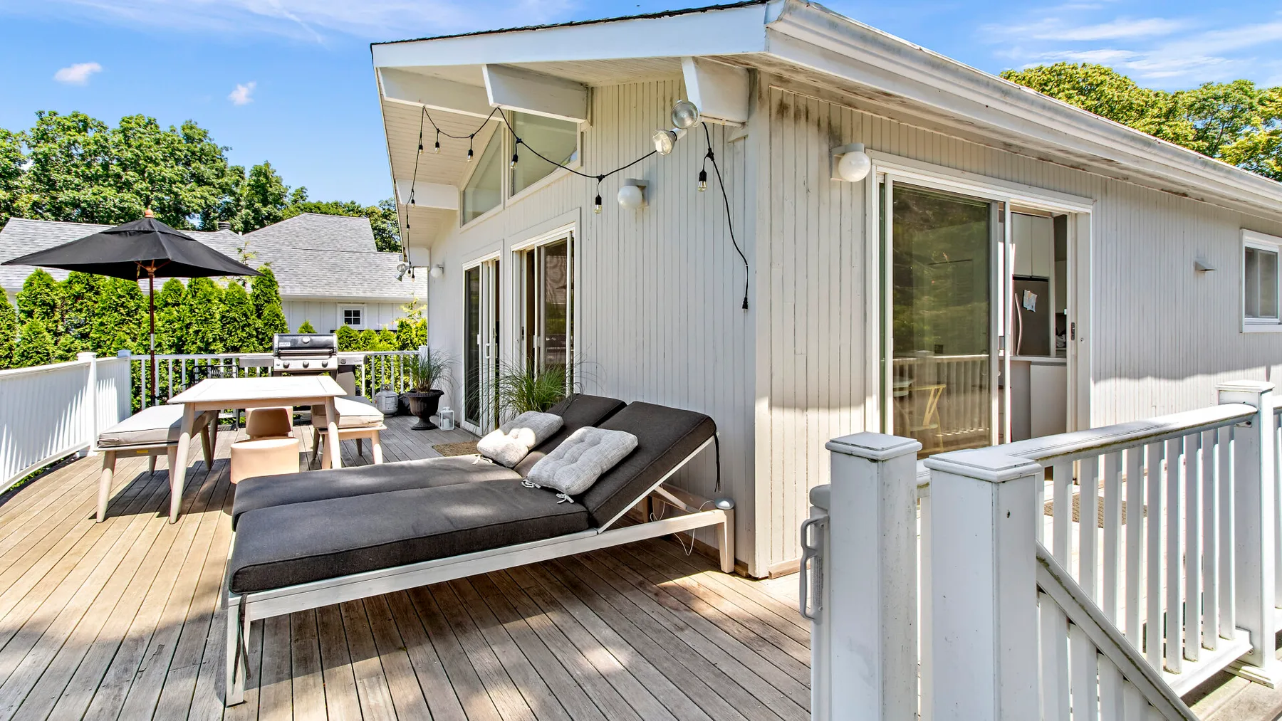 An outdoor deck beside a light-colored house, with lounge seating and a dining table.