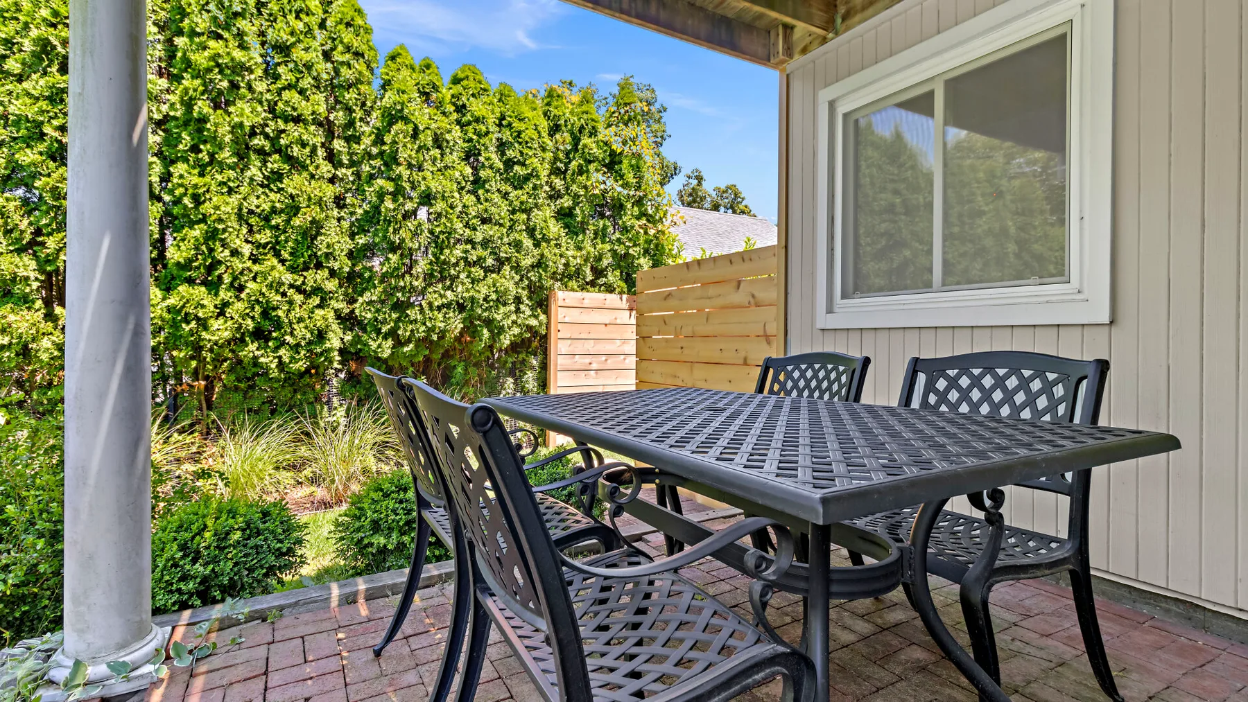 A covered patio with an outdoor dining table and chairs beside a wooden fence.