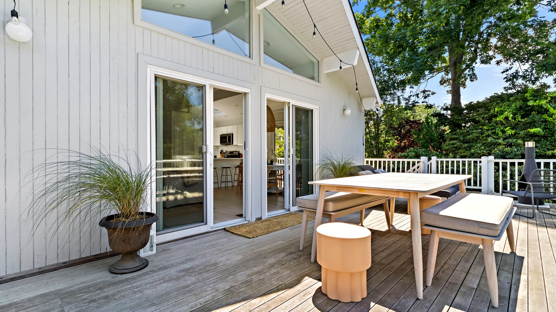 An outdoor deck with a dining table and chairs beside open sliding doors.