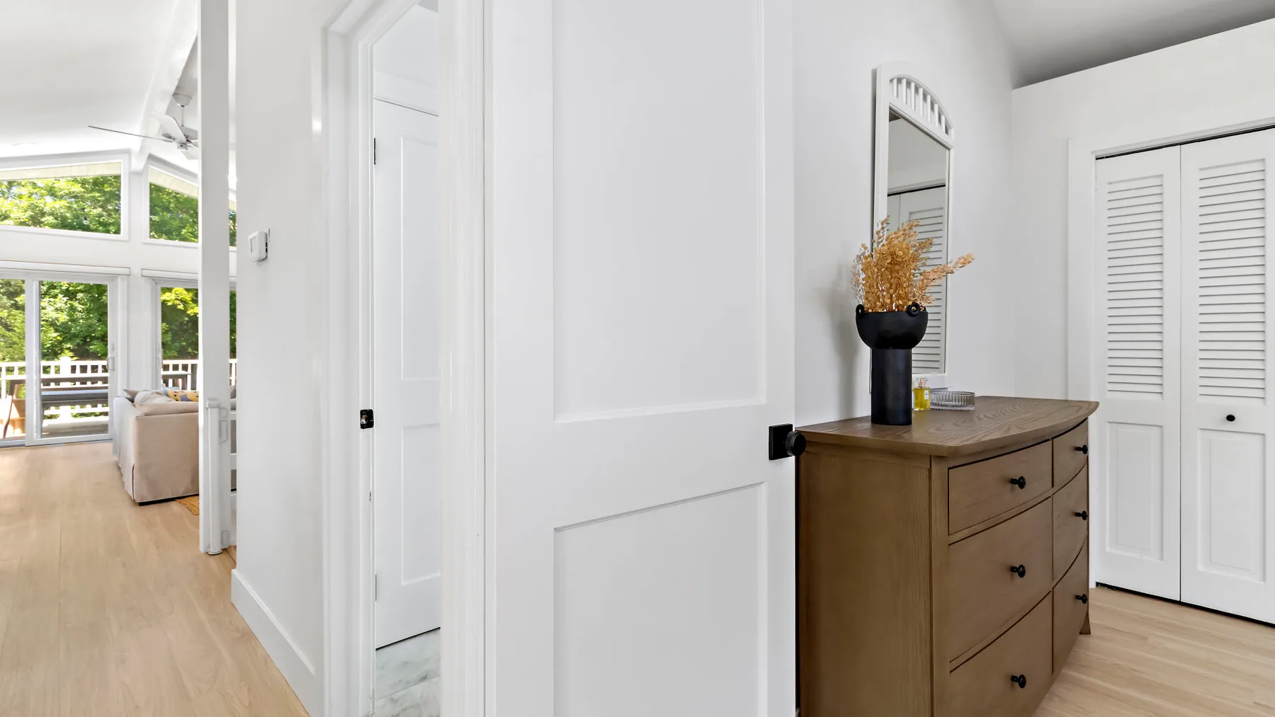 A bright hallway with a wooden dresser and a tall mirror.